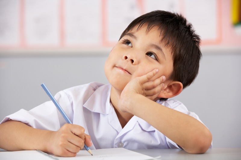 La imagen muestra a un niño con un texto y un lápiz en su mano mirando hacia arriba con gestos de pensamiento