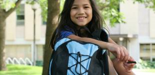 La imagen muestra a una niña con su mochila sentada en un parque