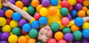 La imagen muestra a un niño sobre muchas pelotas de colores