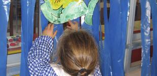 La imagen muestra a una niña pegando un dibujo de un pez en un fondo de plástico azul